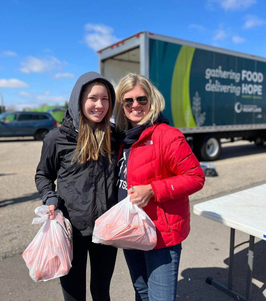 Two volunteers hold bags of food during an outdoor community food distribution.