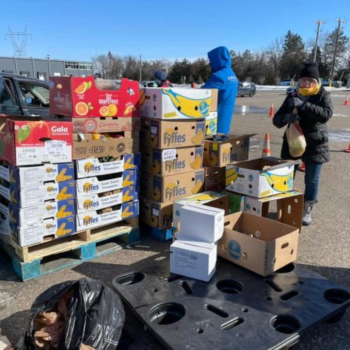 Volunteers distribute boxes of produce from pallets during an outdoor winter food distribution.