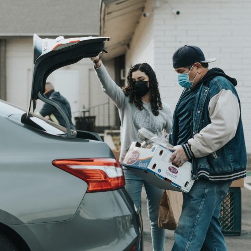 Volunteers place a box of fresh produce into the trunk of a car during a community food distribution.