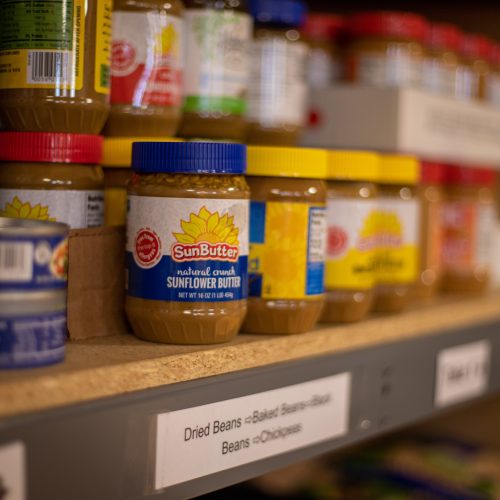 Jars of sunflower butter and canned goods on a pantry shelf labeled dried beans.